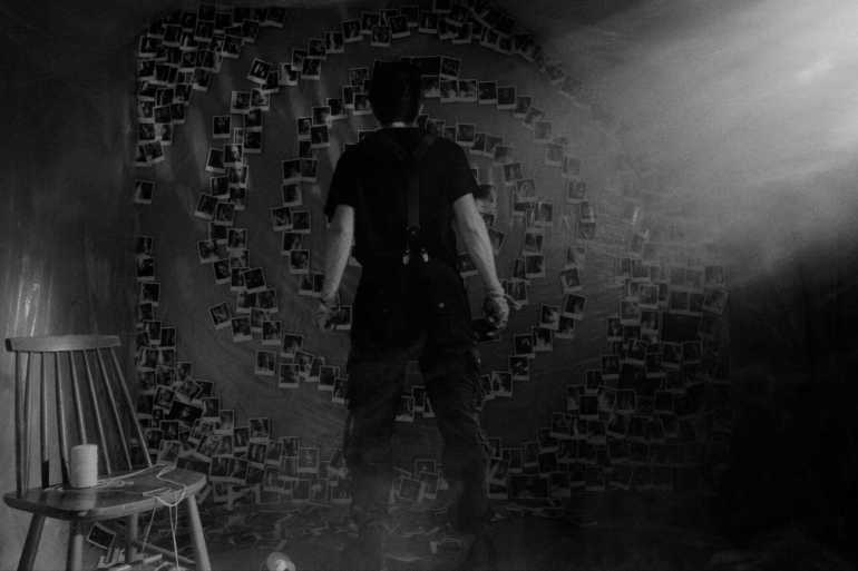 Person standing in front of a spiral of Polaroid photos on a wall.