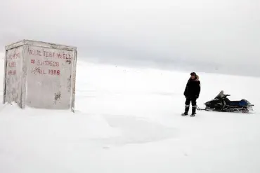 A person standing next to a snowmobile in a snowy, desolate landscape with a weathered structure.