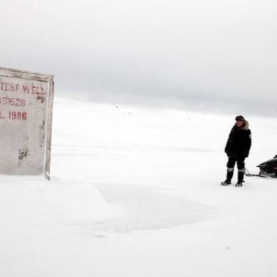 A person standing next to a snowmobile in a snowy, desolate landscape with a weathered structure.