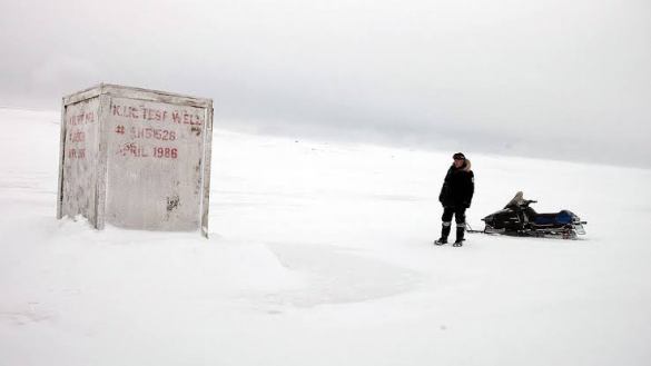 A person standing next to a snowmobile in a snowy, desolate landscape with a weathered structure.
