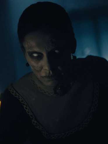 Eerie ghostly figure with glowing eyes in a dark room with candlelight.