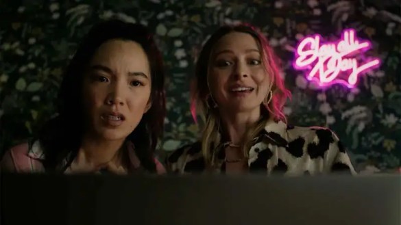 Two women with surprised expressions in front of neon sign reading 'Show and Tell'.