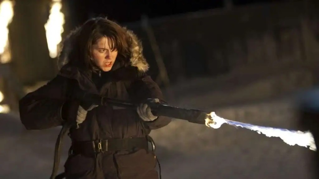 Woman in winter coat fires a flaming torch in a snowy, dark setting.