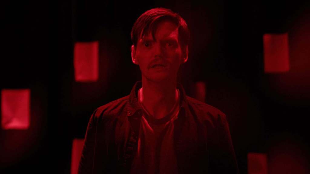 Young man with a serious expression in a dark, red-lit room.