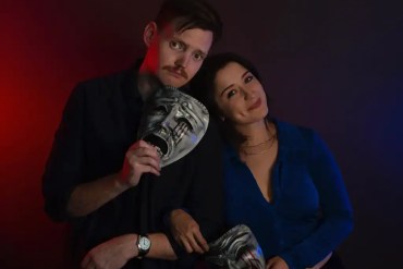 Two people holding horror masks, dark background, dramatic lighting, horror theme.