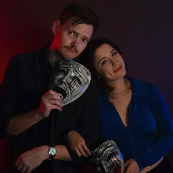 Two people holding horror masks, dark background, dramatic lighting, horror theme.