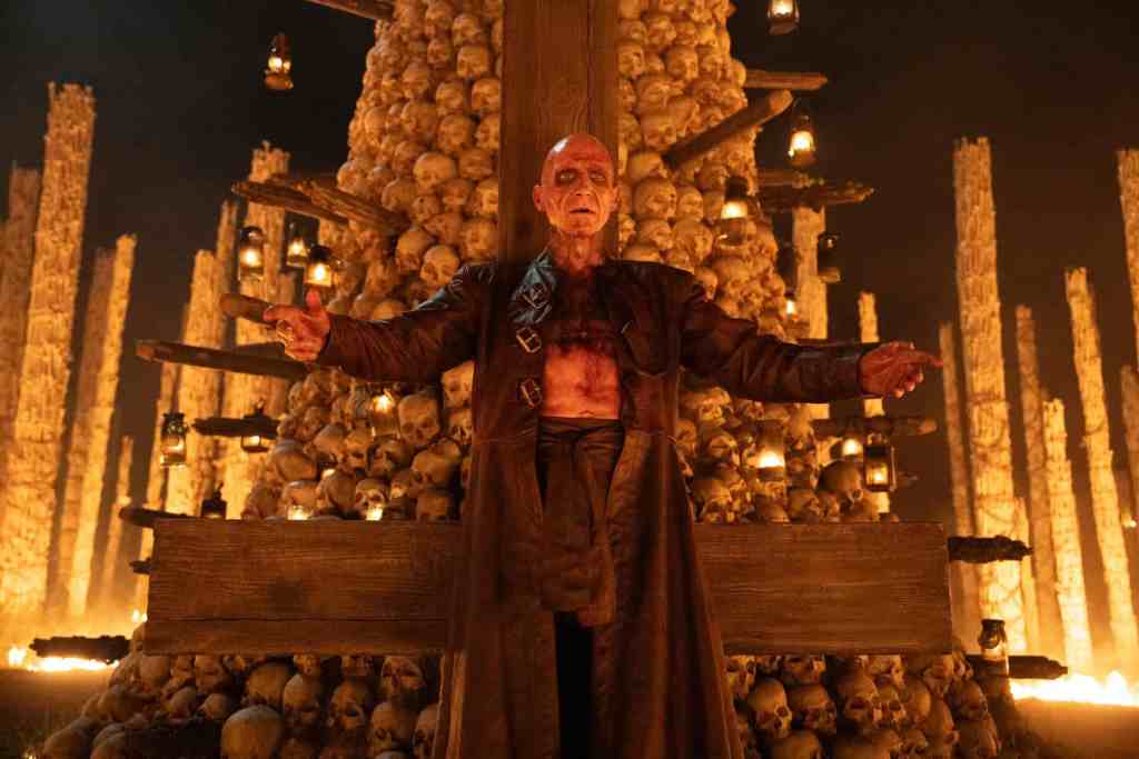 Dramatic scene from horror movie with a man in front of a skull-adorned altar.