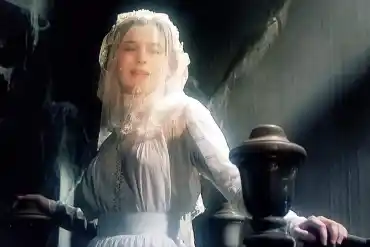 Woman in vintage white dress with veil in dimly lit setting.