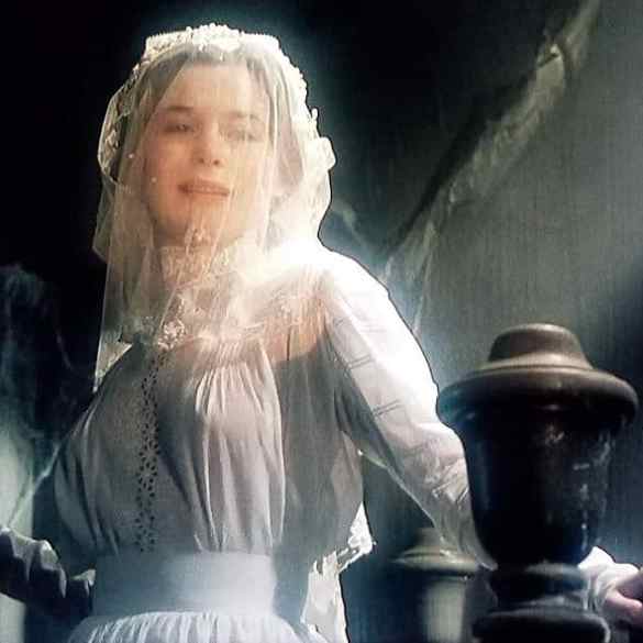 Woman in vintage white dress with veil in dimly lit setting.