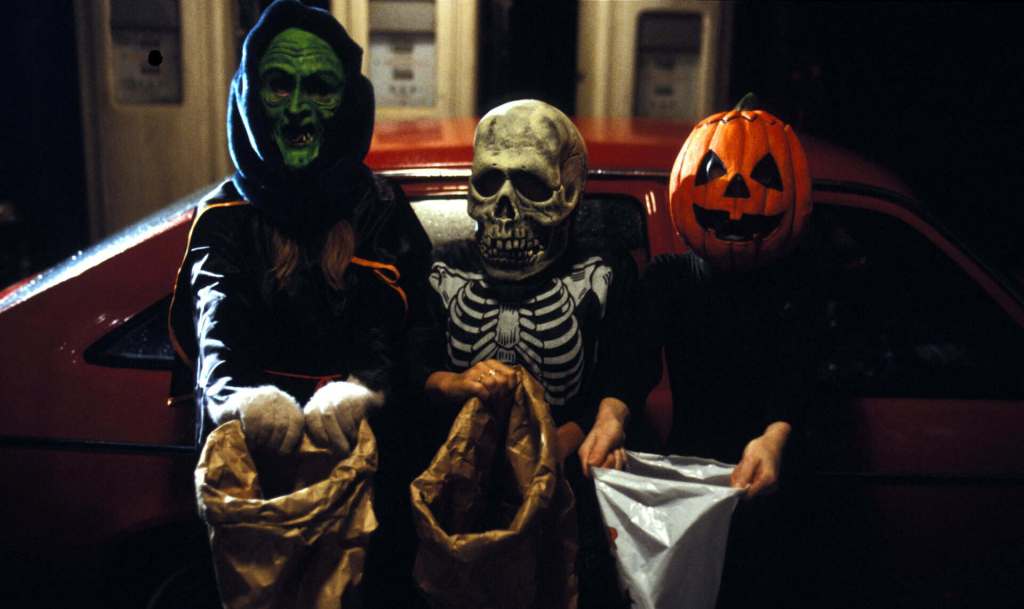 People in Halloween costumes with a skull and pumpkin mask at night.
