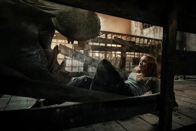 Woman hiding under a table from a monstrous creature in a dark, abandoned setting.