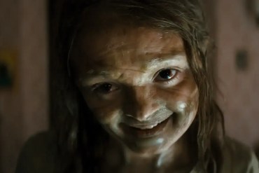 Creepy woman with smeared white face paint and wild hair in a horror scene.