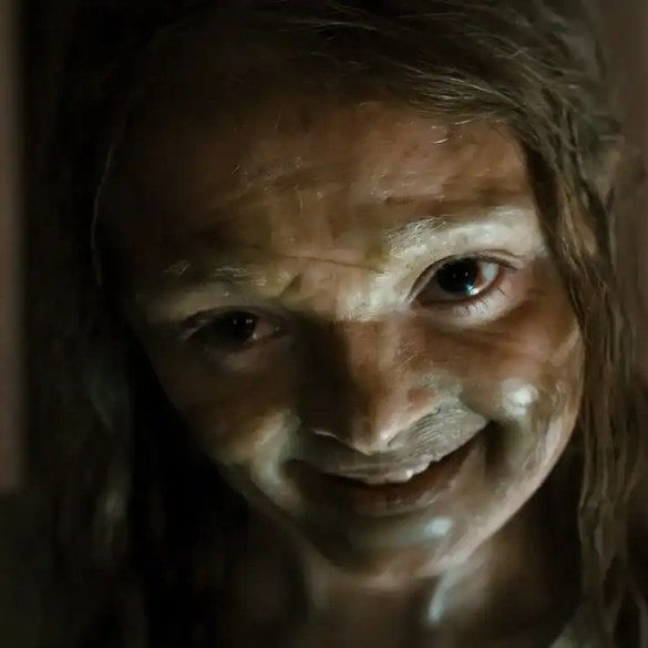 Creepy woman with smeared white face paint and wild hair in a horror scene.