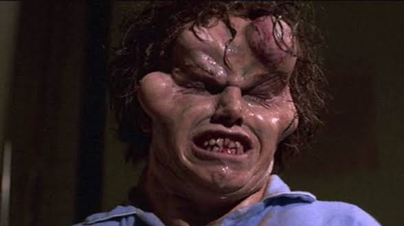 Close-up of a grotesque, distorted face with exaggerated features from a horror film.