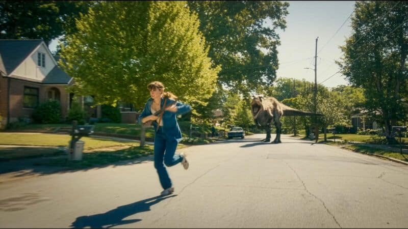 Person running from a dinosaur on a suburban street during daytime.
