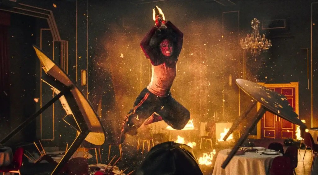 A person in horror costume stands amidst chaos and fire in a haunted house scene.