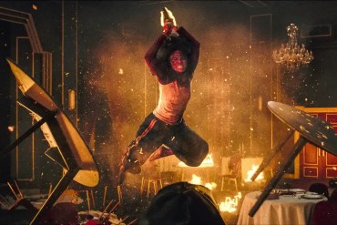 A person in horror costume stands amidst chaos and fire in a haunted house scene.