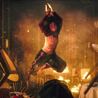 A person in horror costume stands amidst chaos and fire in a haunted house scene.