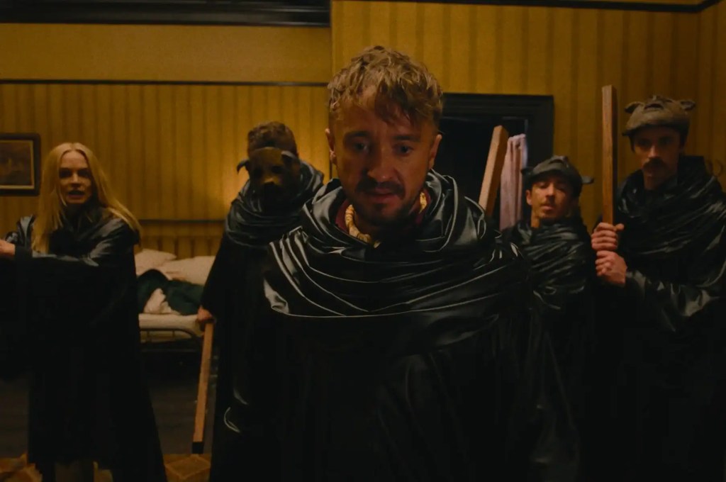 Group of people in dark costumes with masks in a dimly lit room.