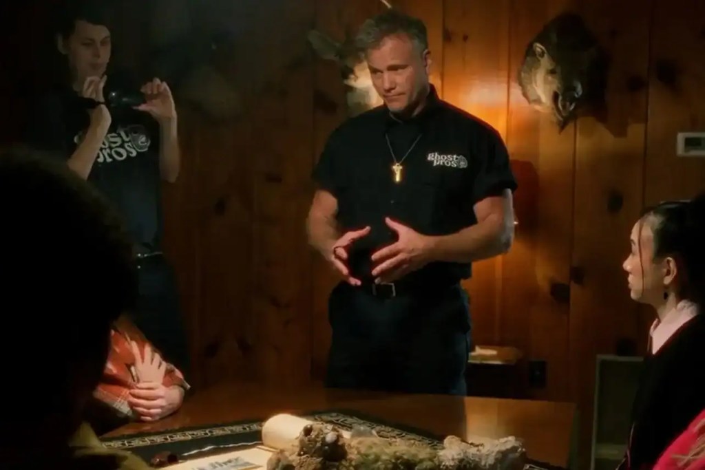 Man in black shirt explaining to group in wood-paneled room at Popcorn Frights FF.