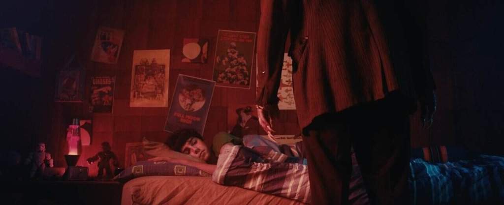 A person lying on a bed in a dimly lit room with posters on the wall.