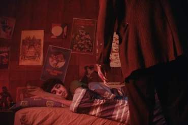 A person lying on a bed in a dimly lit room with posters on the wall.