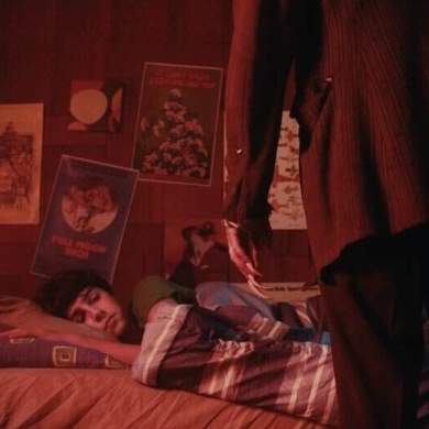 A person lying on a bed in a dimly lit room with posters on the wall.