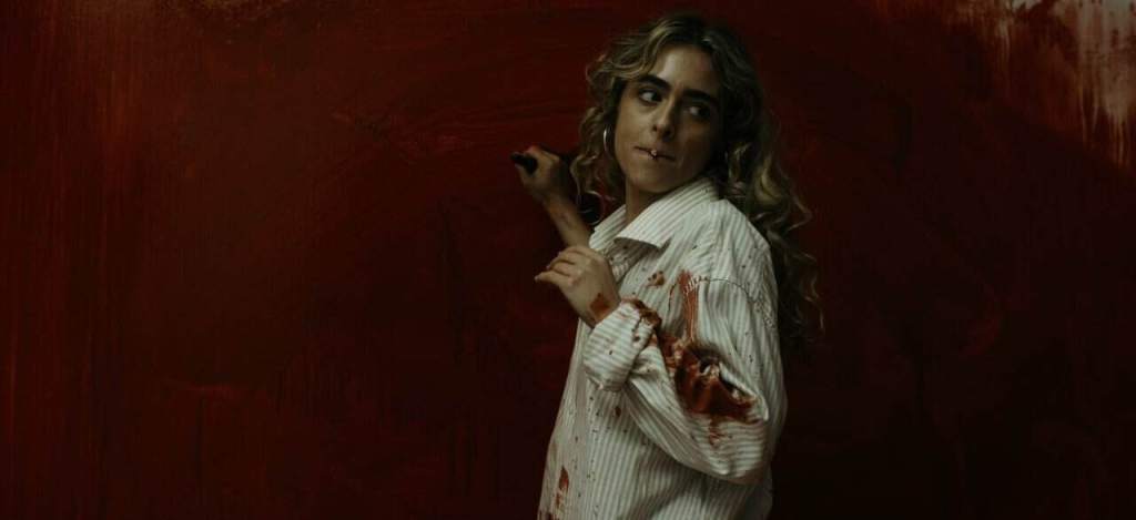 Woman in bloodstained white shirt holding a knife against a dark red background.