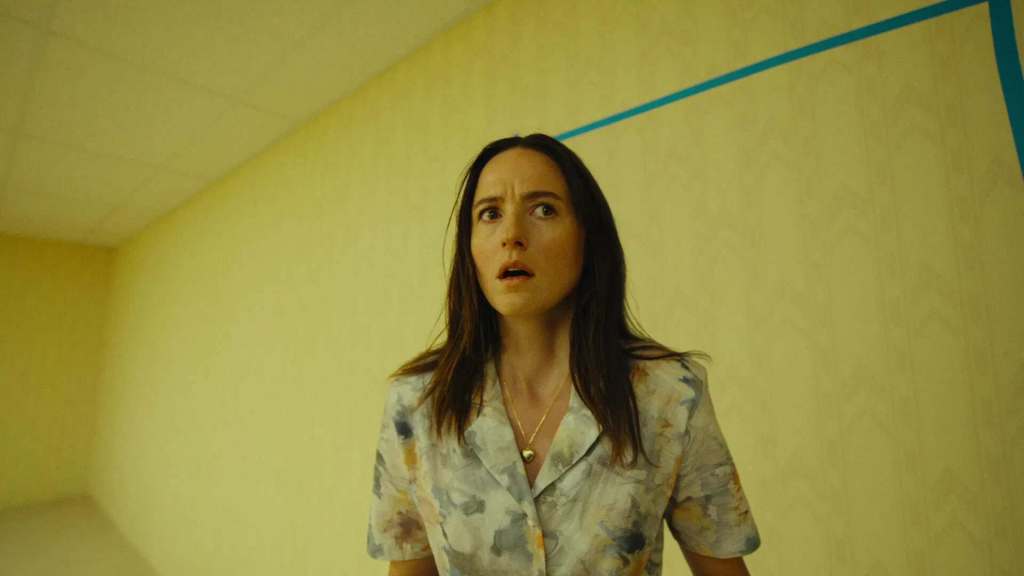 Woman with surprised expression in a yellow room with blue lines.