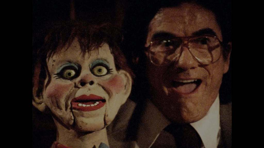 Creepy ventriloquist dummy with a smiling man in a dark setting.