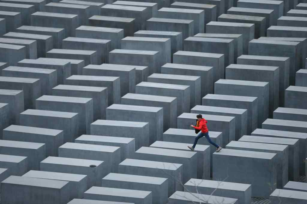 Person in red jacket crossing a maze of concrete blocks in an urban landscape.