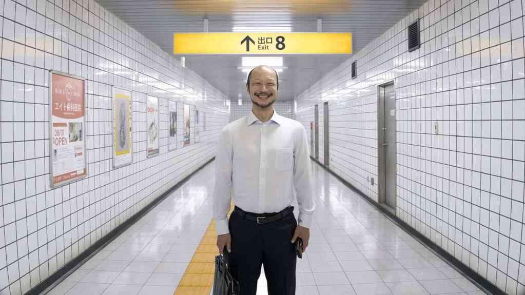 Smiling man in white shirt in subway corridor with yellow signage.