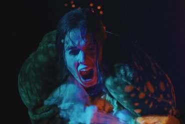 Scary creature with blue face and open mouth in dark setting.