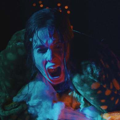 Scary creature with blue face and open mouth in dark setting.