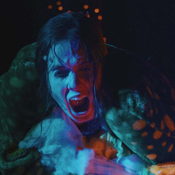 Scary creature with blue face and open mouth in dark setting.