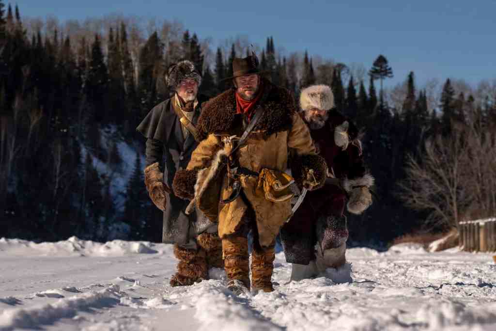 Three explorers walking through snow in a winter landscape with trees.
