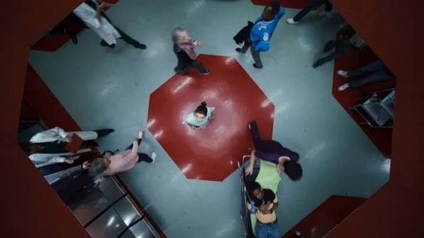 People gathered around a central octagonal red floor in a busy indoor setting.