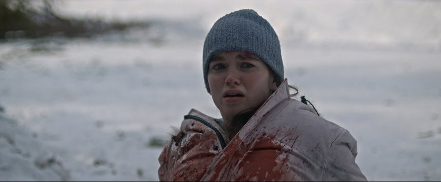 Young girl in winter coat and gray beanie looks frightened in snowy landscape.