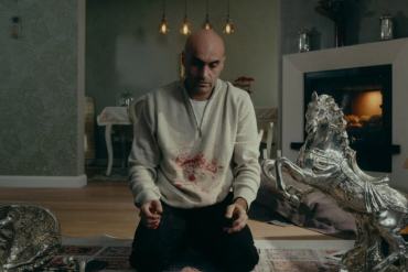 Man kneeling in a living room with silver sculptures and a fireplace.