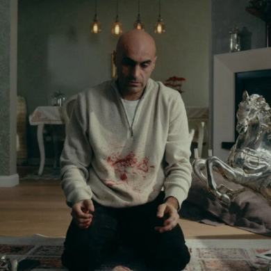 Man kneeling in a living room with silver sculptures and a fireplace.