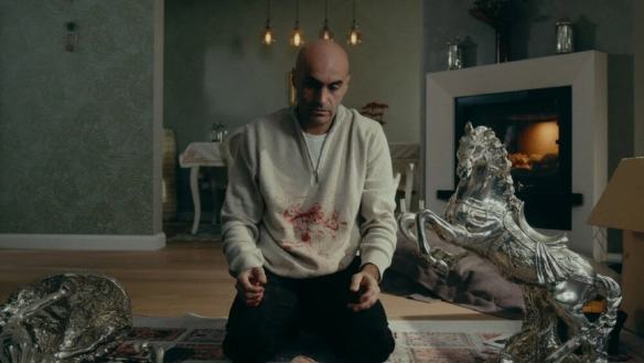 Man kneeling in a living room with silver sculptures and a fireplace.