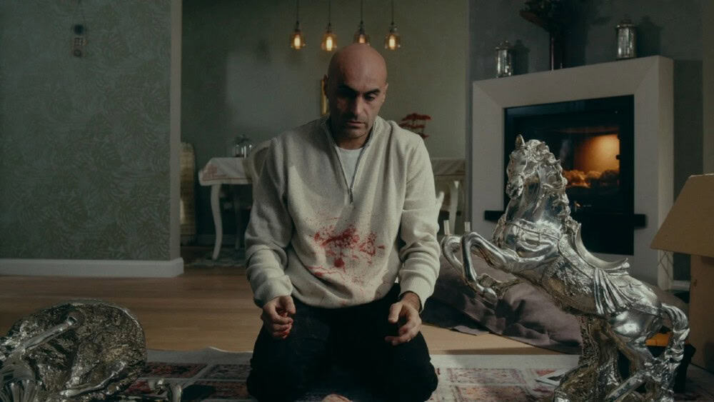 Man kneeling in a living room with silver sculptures and a fireplace.