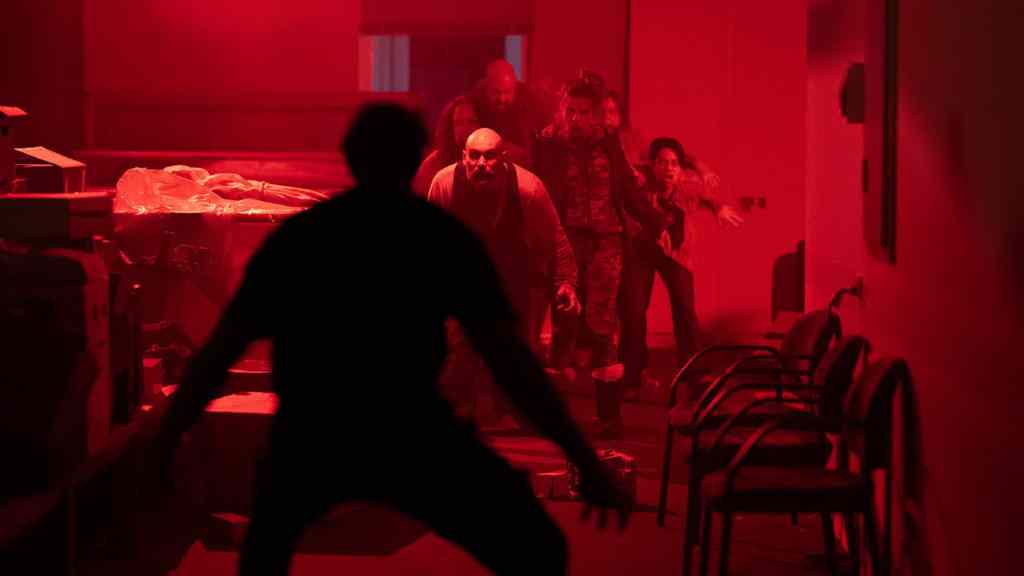 Group of people walking through a dimly lit, red-tinted room with chairs and tables.