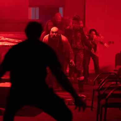 Group of people walking through a dimly lit, red-tinted room with chairs and tables.