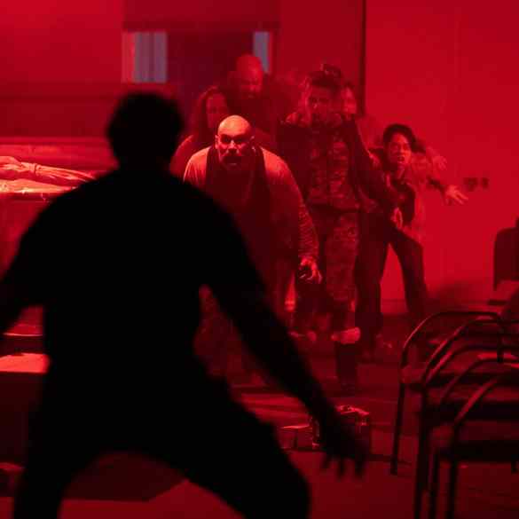 Group of people walking through a dimly lit, red-tinted room with chairs and tables.