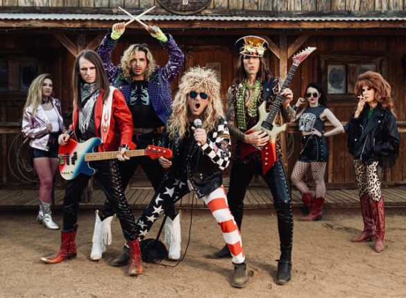 Rock band dressed in eclectic costumes performing outdoors at a rustic venue.