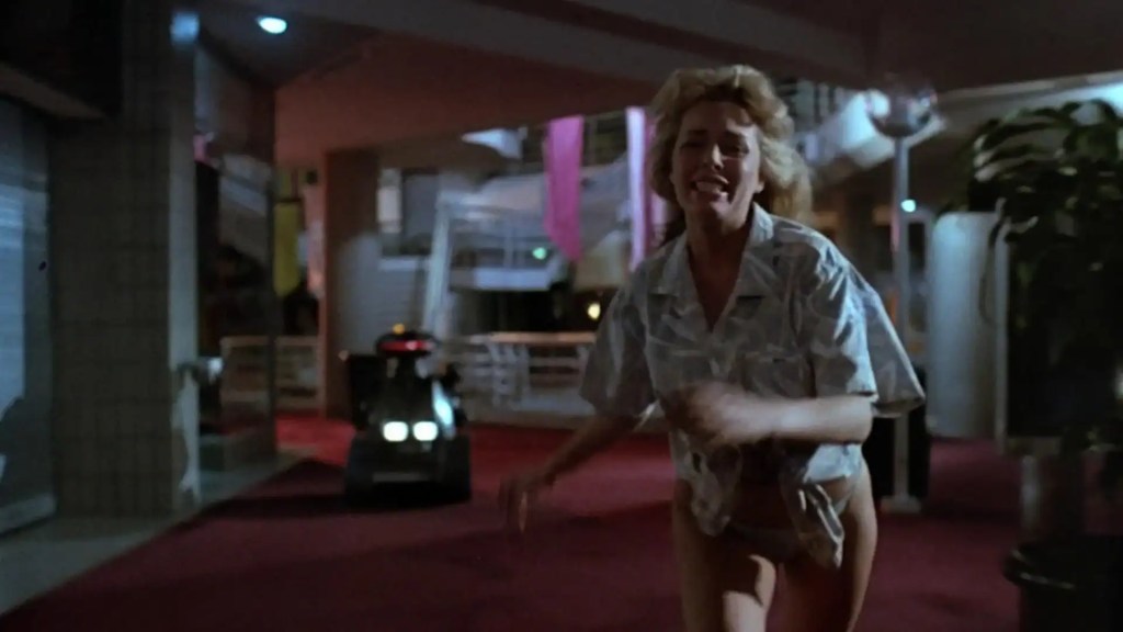 Woman running in a parking garage at night, looking scared and distressed.