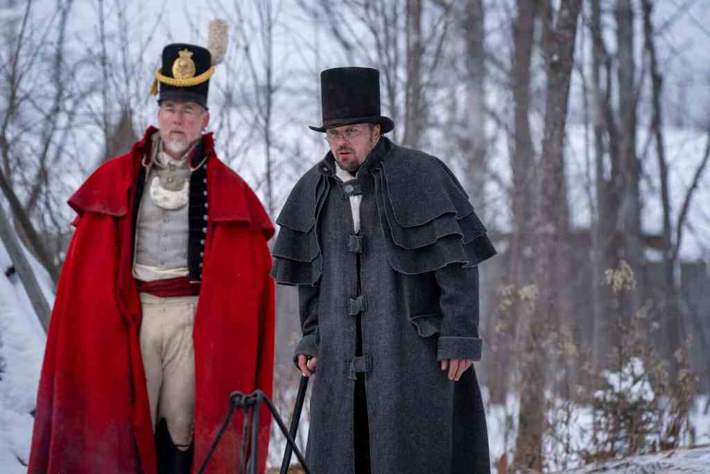 Two men in historical costumes stand outdoors in a snowy forest.