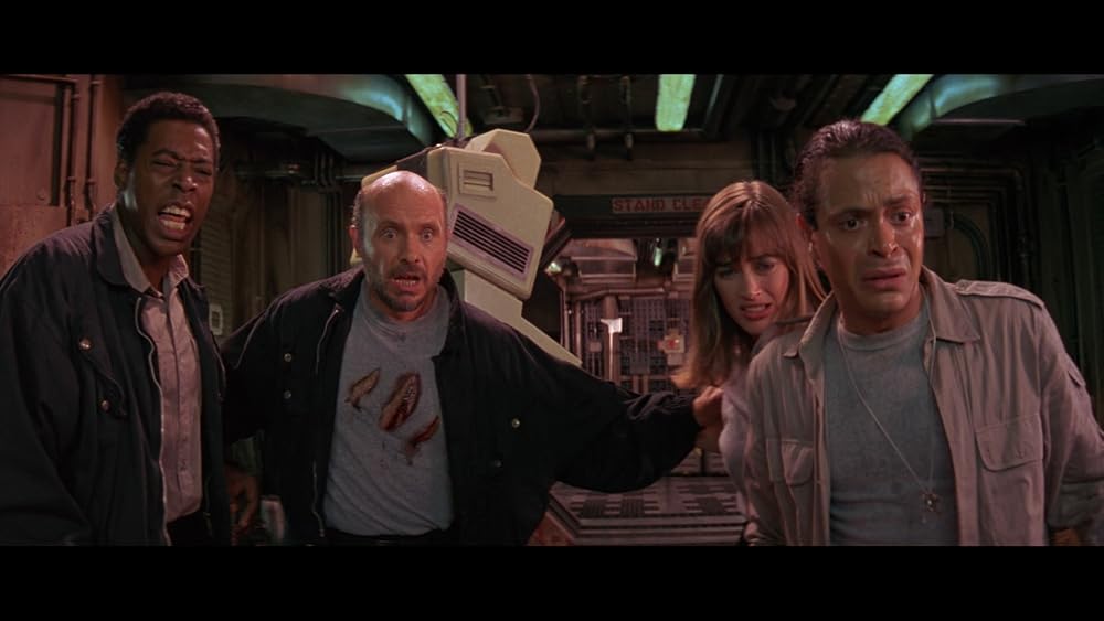 Scene from a horror movie with four frightened characters in a spaceship corridor.