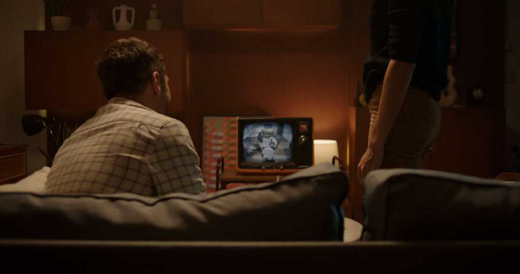 Two adults watching a vintage TV on a dimly lit sofa scene from The Me in the TV.